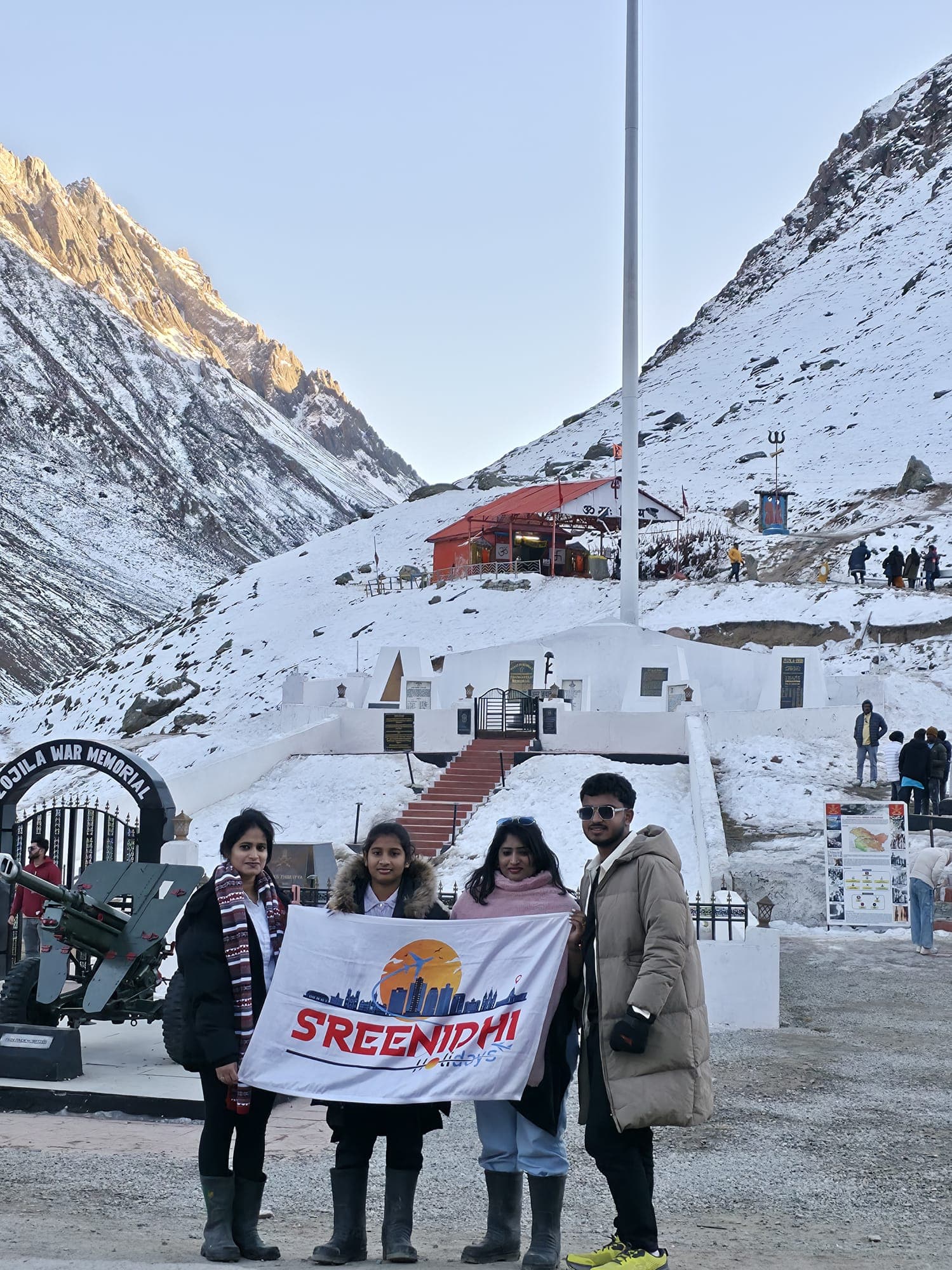 Travellers with the Sreenidhi Holidays banner at the snow-covered Zojila War Memorial