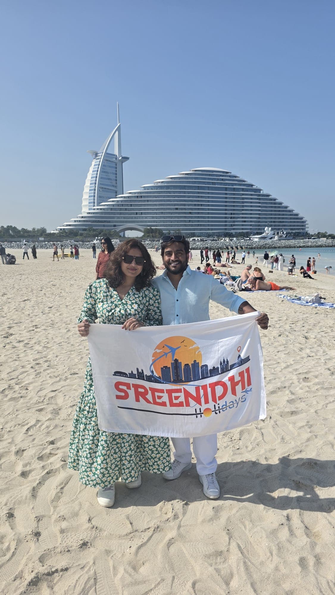 Couple with the Sreenidhi Holidays banner on the beach by the Burj Al Arab, Dubai